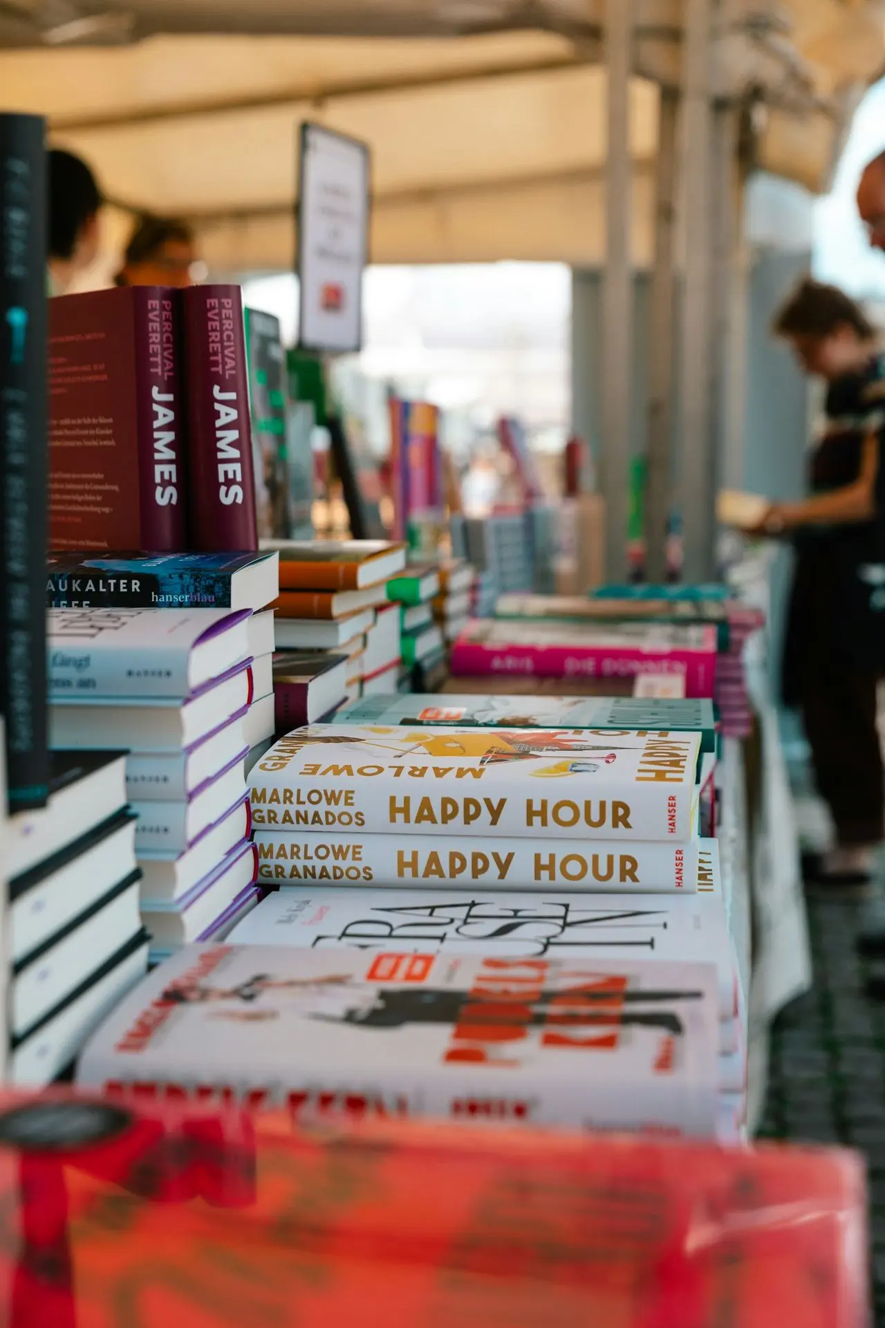 A number of books on a table with people in the background